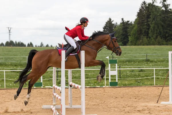 Horsewoman in red jacket is jumping over a hurdle — Stock Photo, Image