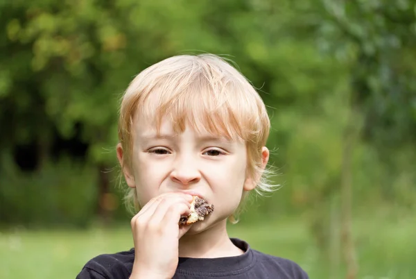 Der blonde Junge isst einen Kuchen — Stockfoto