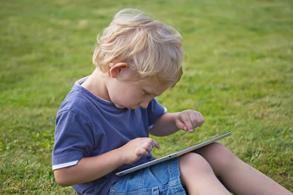 El chico rubio está jugando con la tableta de PC al aire libre —  Fotos de Stock