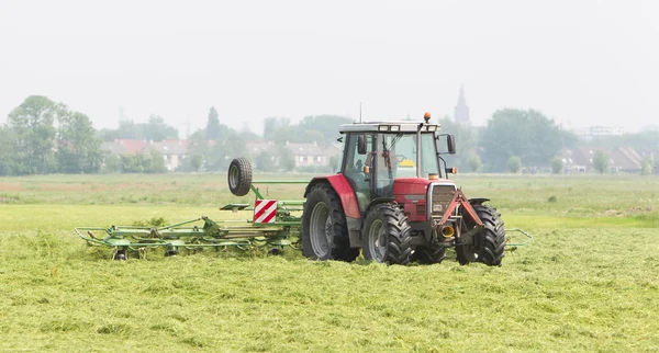 Rolnik używa ciągnika do rozprzestrzeniania się siano na polu — Zdjęcie stockowe