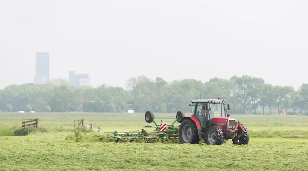 Rolnik używa ciągnika do rozprzestrzeniania się siano na polu — Zdjęcie stockowe