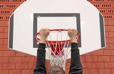 Okulun spor salonunda sepette asılı duran adam, kırmızı tuğla duvar.