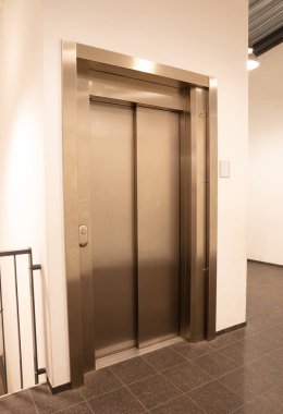 Modern ofis parçası, beyaz bir duvarda parlayan asansör kapıları.