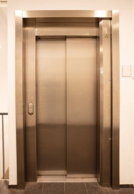 Modern ofis parçası, beyaz bir duvarda parlayan asansör kapıları.