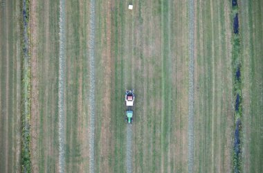 Tarım traktörü tarım için biçilmiş çimenleri topluyor ve saman balyalarını plastik bir alanda, Friesland 'da paketliyor.