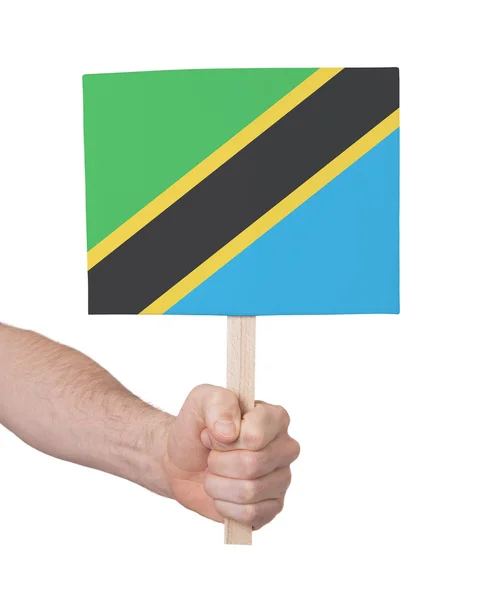 Mão segurando cartão pequeno - Bandeira da Tanzânia — Fotografia de Stock