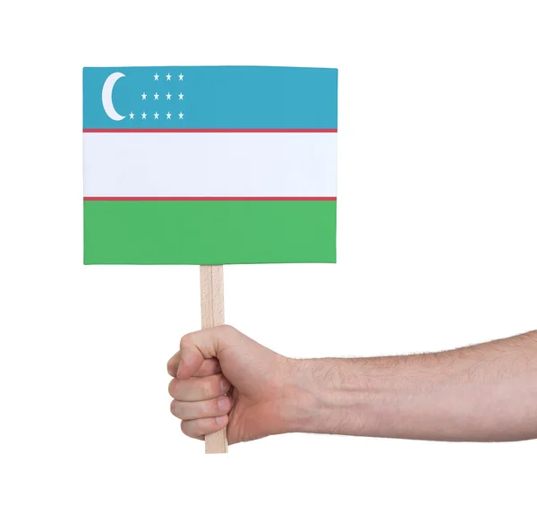 Mano sosteniendo una tarjeta pequeña - Bandera de Uzbekistán —  Fotos de Stock