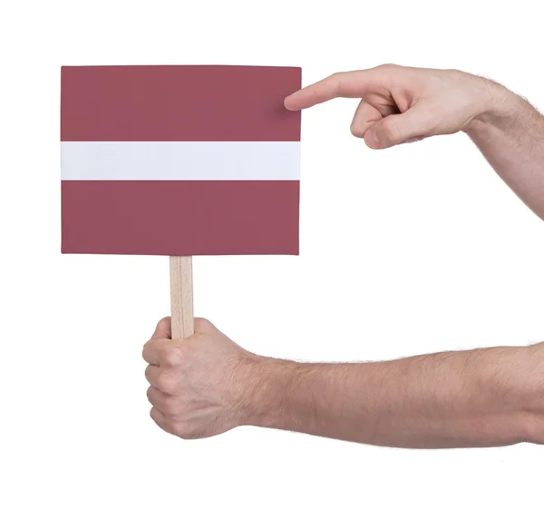 Mano con tarjeta pequeña - Bandera de Letonia — Foto de Stock