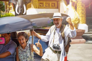 Kıdemli Amerikan turist çifti, Tuk Tuk Tayland taksisiyle Tuk Tuk Thailand Tapınağı 'nın güneşli arka planında fotoğraf çekerken komik gülücükler ve kahkahalar gösteriyor. Kıdemli turist konsepti