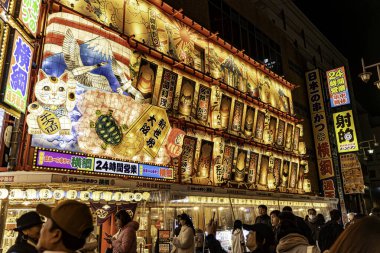 Osaka şehri, Japonya - 07 Aralık 2024: Kentin gece manzarası ve Shinsekai bölgesinde kalabalık olan Japonca ilginç tabela. Shinsekai caddesi, caddenin her iki tarafında da turnuva yapan dükkanlar ve restoranlarla dolu.