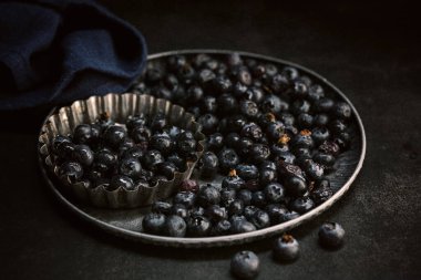 Koyu arkaplanda bir tepside çiğ yaban mersini.