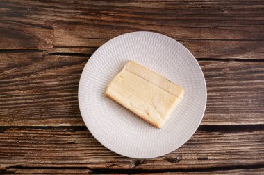 Tahta bir masada beyaz bir tabakta sade raclette peyniri.