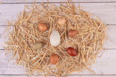 Çeşitli boyutlarda ve renkte yumurtalar ve ahşap bir masanın üzerinde saman.