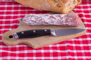 Kırmızı bir masa örtüsünün üzerindeki tahta kesme tahtasındaki sosis.