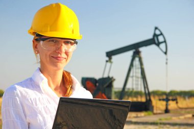 Başarılı bir kadın mühendis, bir defter ile petrol pompasını kontrol ediyor, güvenlik gözlüklü, gülümseyen genç bir bayanı yakından kontrol ediyor.