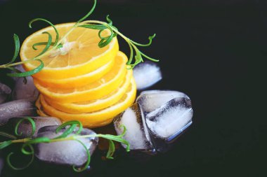 Taze dilimlenmiş limon, siyah arka planda bir tutam biberiye ve buz..