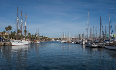 BARCELONA, İspanya - 7 Aralık 2023: eski Barcelona limanı, liman ve yatlar kenetlendi. Uzun direkli büyük bir gemi solda, daha küçük yatlar sağda. Arka planda palmiye ağaçları ve binalar görülebilir.