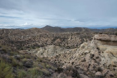 İspanya, Almera 'daki Tabernas Çölü' nün kurak manzarası, engebeli tepeler, seyrek bitki örtüsü ve bulutlu bir gökyüzü altında kayalık çıkıntılar. Popüler bir çekim yeri.