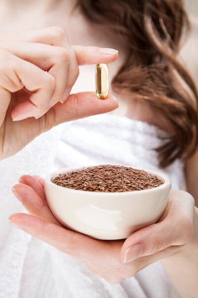 Woman hand holding bowl of flax seeds and Omega-3 capsule