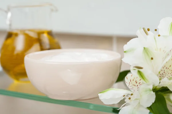 Натуральное масло, питательная маска и цветы на полке ванной комнаты — стоковое фото