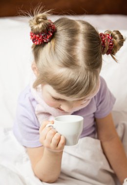 Little girl sitting in a bed with cup clipart