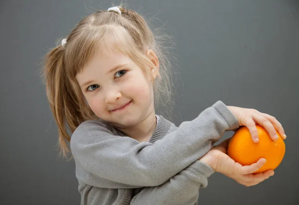 Улыбающаяся маленькая девочка держит спелый апельсин — стоковое фото
