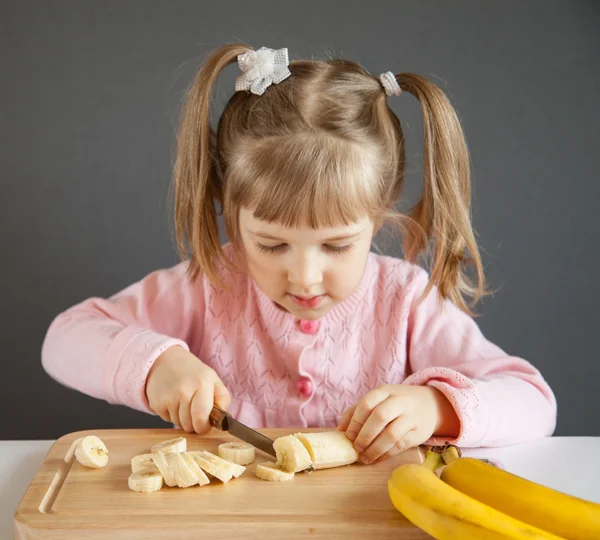 Kleines Mädchen schneidet eine reife Banane — Stockfoto