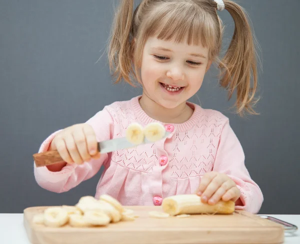 Little girl cutting a ripe banana — Stock Photo, Image