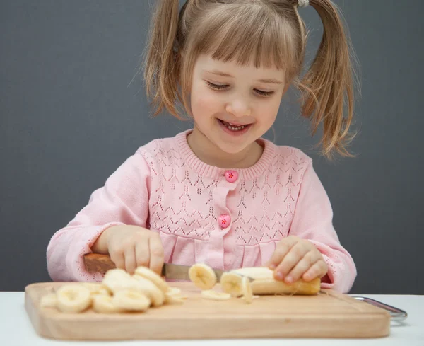 Маленькая девочка режет спелый банан — стоковое фото