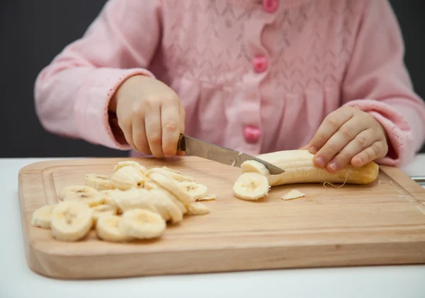Little girl cutting a ripe banana — Stock Photo, Image