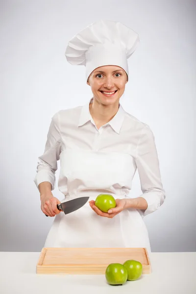 Hermosa joven cocinera mostrando una manzana verde — Foto de Stock