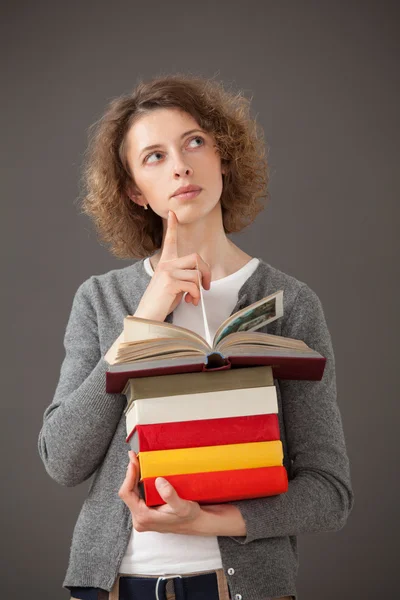 Вдумчивая молодая женщина держит стопку книг — стоковое фото