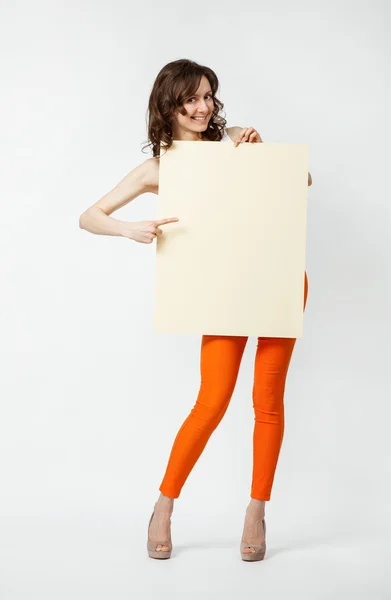 Playful young woman in orange pants holding blank placard showin — Stock Photo, Image