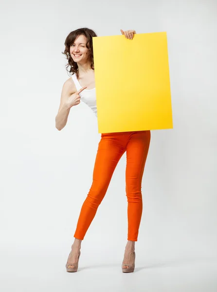 Playful young woman in orange pants holding blank yellow placard — Stock Photo, Image