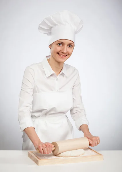 Beautiful young female cook rolling out dough on wooden board — Stock Photo, Image