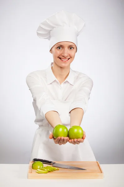 Hermosa joven cocinera mostrando una manzana — Foto de Stock