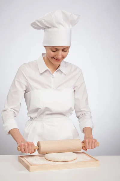 Beautiful young female cook rolling out dough on wooden board — Stock Photo, Image