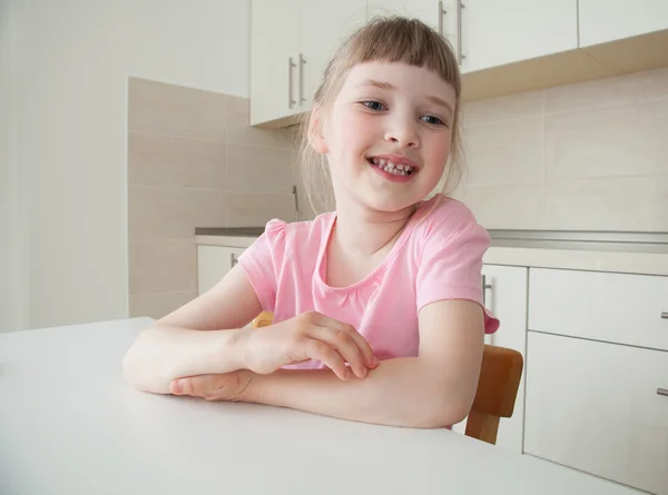 Glückliches kleines Mädchen sitzt am Tisch — Stockfoto