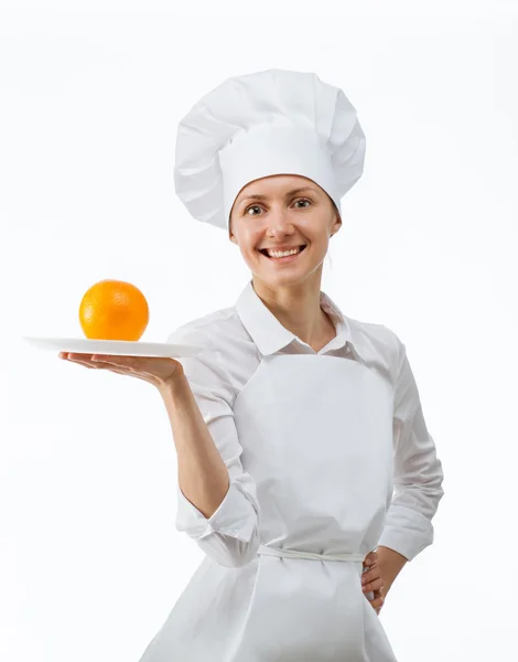 Hermosa joven cocinera mostrando naranja en un plato — Foto de Stock