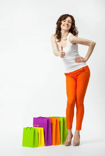 Gelukkig jonge lachende brunette in oranje broek met shopping tassen — Stockfoto
