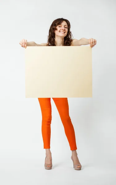 Joyful young woman in orange pants holding blank placard — Stock Photo, Image