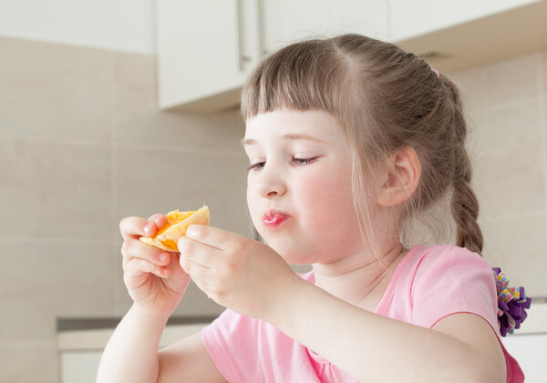 Happy little girl eating a tasty orange 