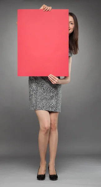 Smiling young woman peeping out through a red placard — Stock Photo, Image