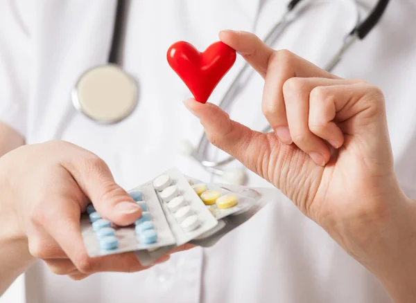 Médico segurando comprimidos e coração — Fotografia de Stock