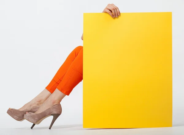 Неузнаваемая молодая женщина в оранжевых штанах держит желтую бумагу — стоковое фото
