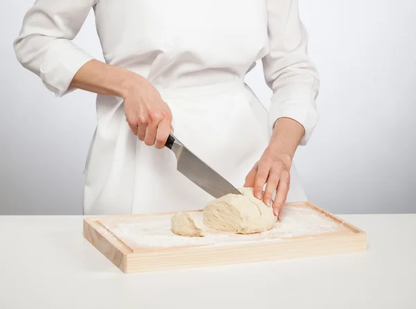 Женщина-повар режет сырое тесто — стоковое фото