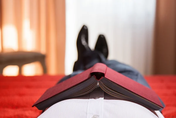 Entspannter Herr liegt mit Buch auf dem Bett — Stockfoto