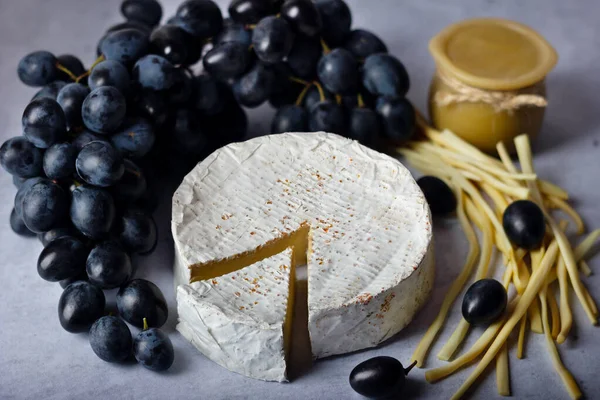 Assorted cheeses Camembert, smoked cheese with black grapes and honey on stone background