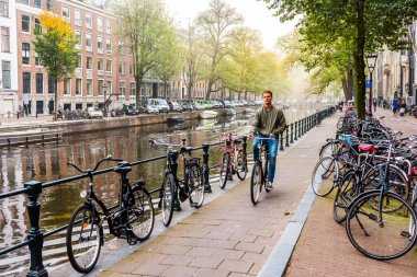 AMSTERDAM, NETHERLANDS - 24 Eylül 2017: Amsterdam caddesinde bisiklet süren genç adam. Hollanda.