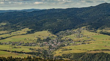 Geniş bir hava manzarası, ormanlı tepeler ve geniş çayırlarla çevrili, dağlık bir vadide yuva yapmış küçük bir köyü gösteriyor. Kırsal yaşamı, sükuneti ve dağlık kırsal kesimin güzelliğini yakalıyor..